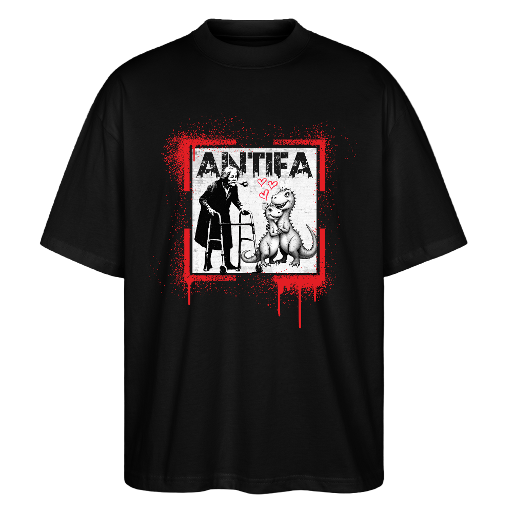 Front view black T‑shirt showing a person using a walker facing a seated dinosaur with pink hearts between them, framed by red paint splatter and distressed white “ANTIFA” print above.